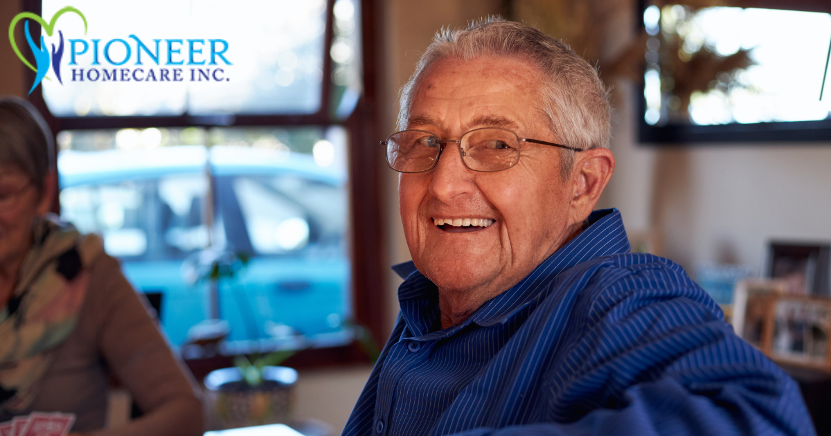 A happy, smiling senior man sitting at a table and looking over his shoulder, enjoying life as a result of successful long-distance caregiving.