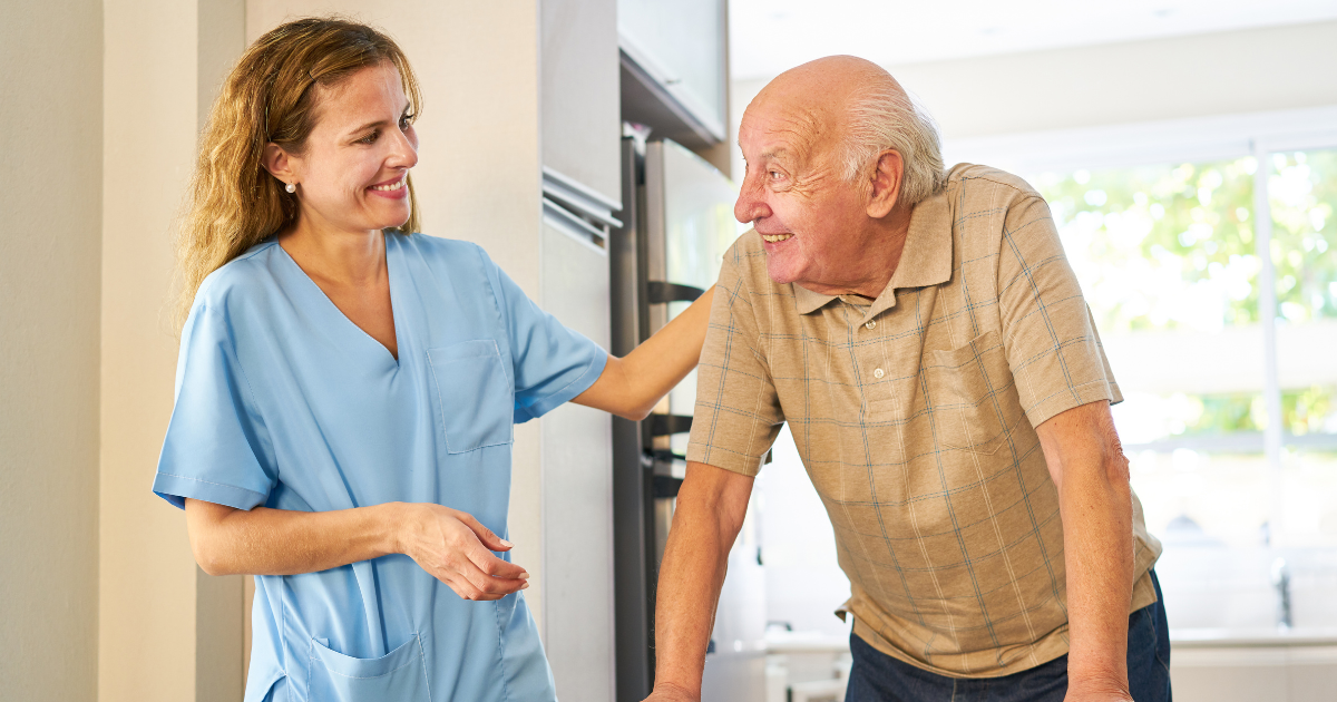 Caregiver providing senior home care smiling at senior man using a walker