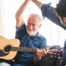 A smiling son high fives his happy elderly father as he plays the guitar, showing the positive effect music can have on people, including those with dementia.